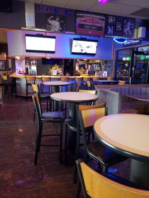 An indoor bar and lounge area with high-top tables, barstools, and televisions mounted on the wall.