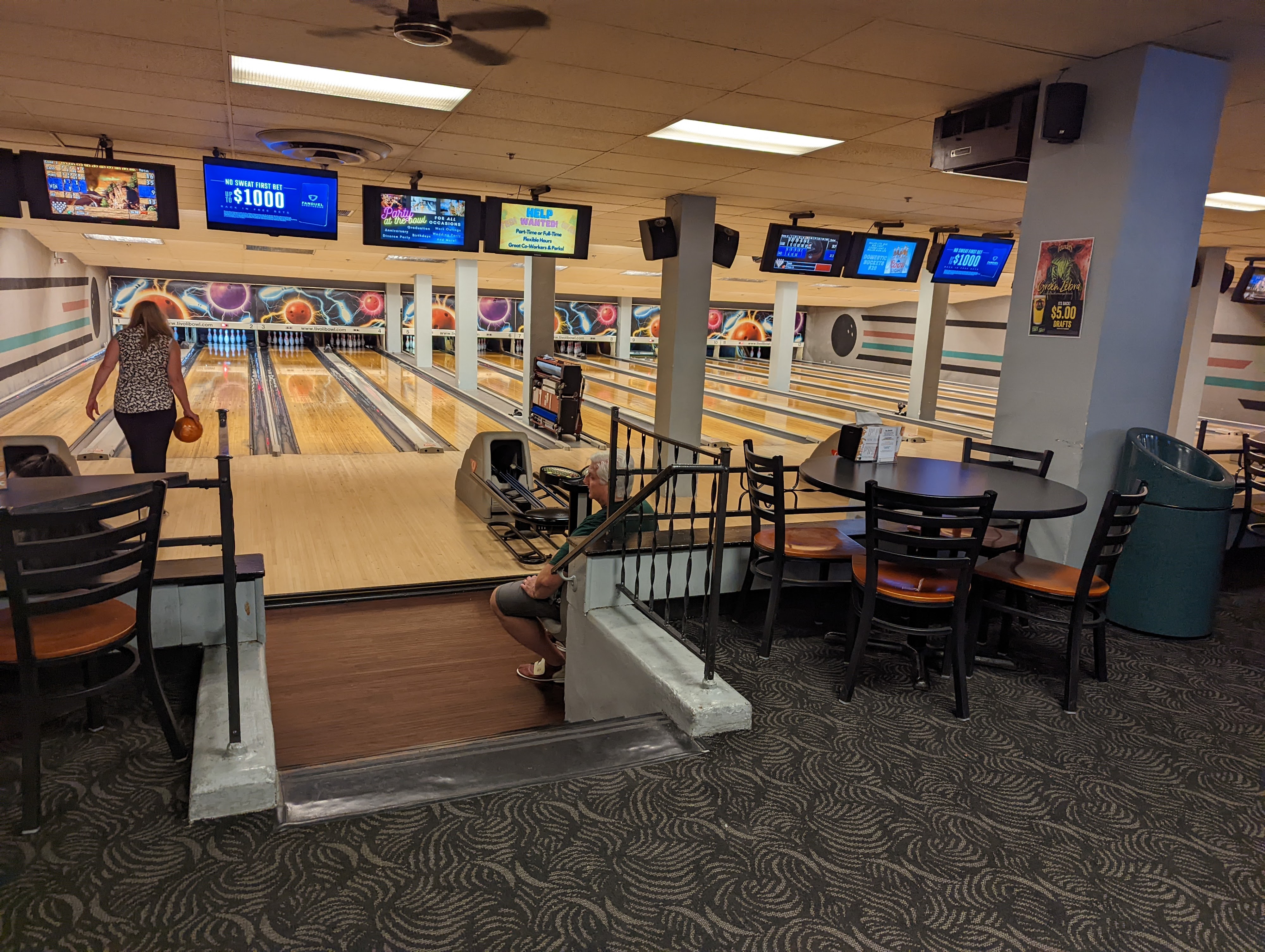 Wide interior view of bowling lanes, scoring monitors, and a seating area at Tivoli Bowl.