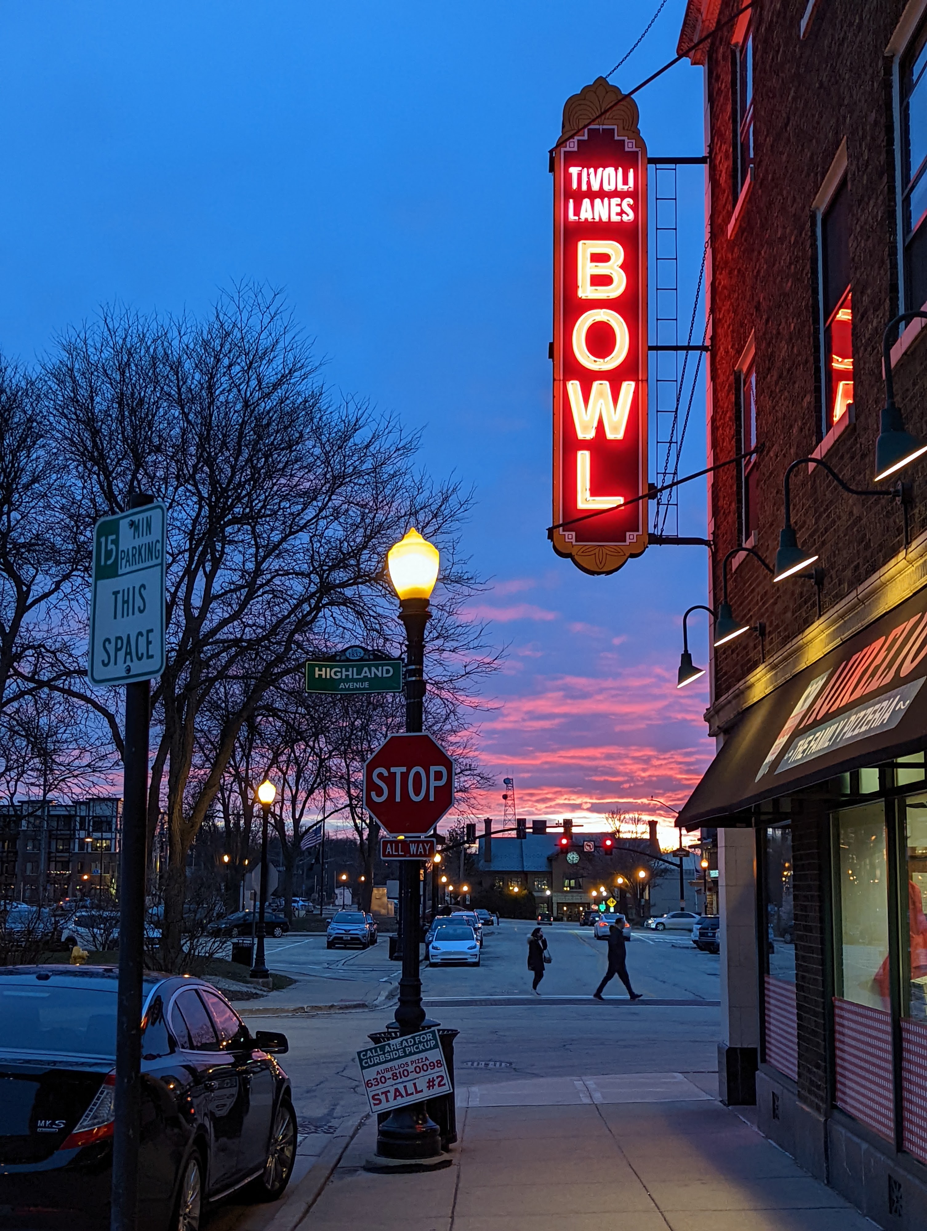 A vertical red neon sign for Tivoli Lanes BOWL against a vibrant pink and orange sunset sky.