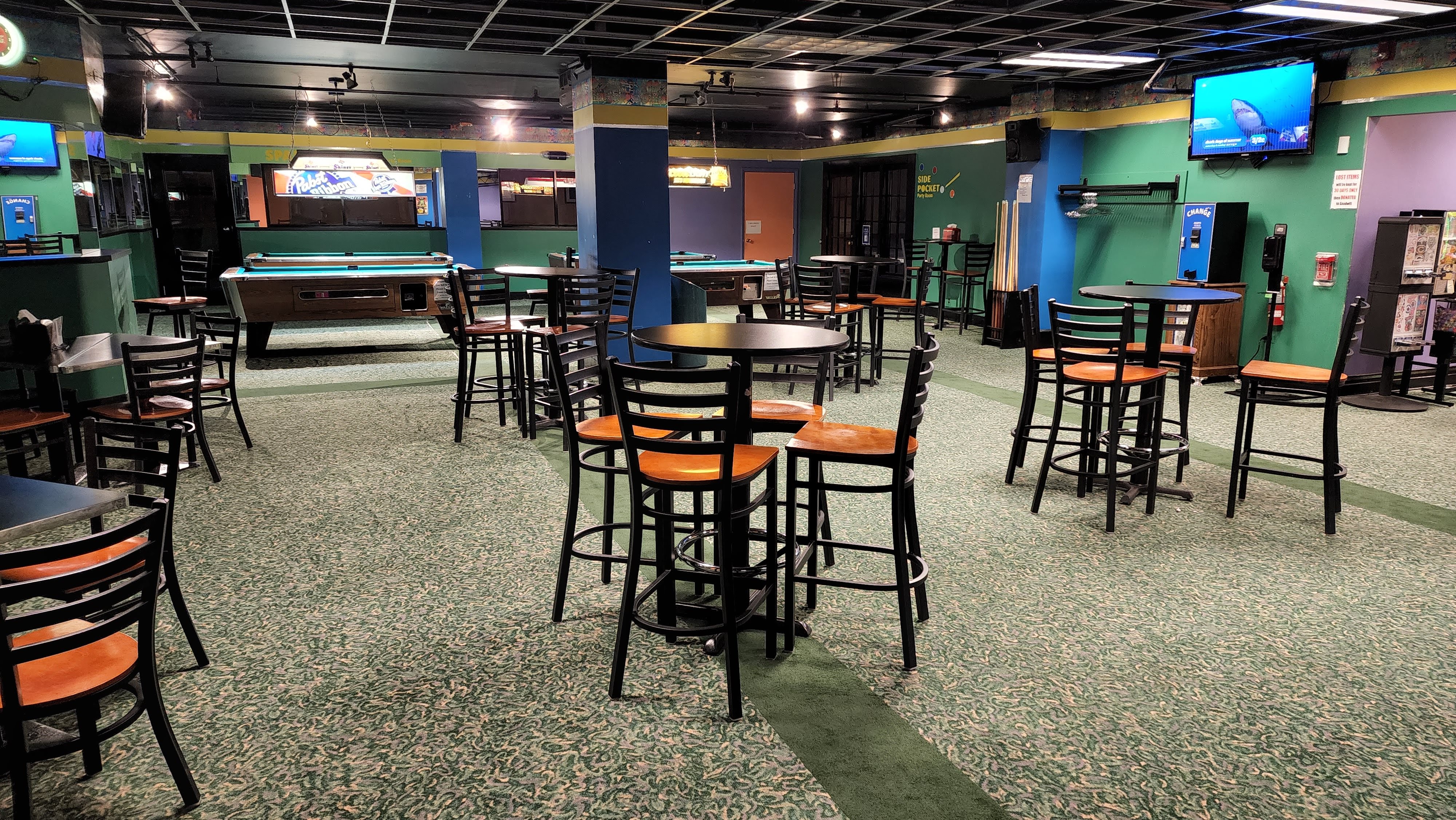 A lounge area with several high-top tables and chairs in front of billiards tables.