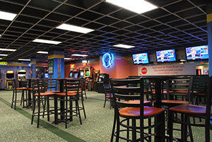 A lounge area with high-top tables, bar stools, arcade games, and wall-mounted televisions.