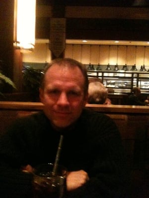 A man sitting at a restaurant table with a drink in a dimly lit lounge area.