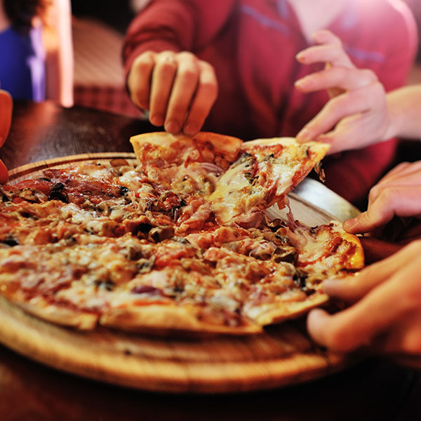 A close-up of several hands taking slices of a hot pizza from a wooden serving board.