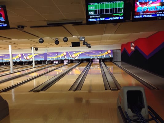 A wide view of polished bowling lanes with overhead scoring monitors and colorful wall graphics.