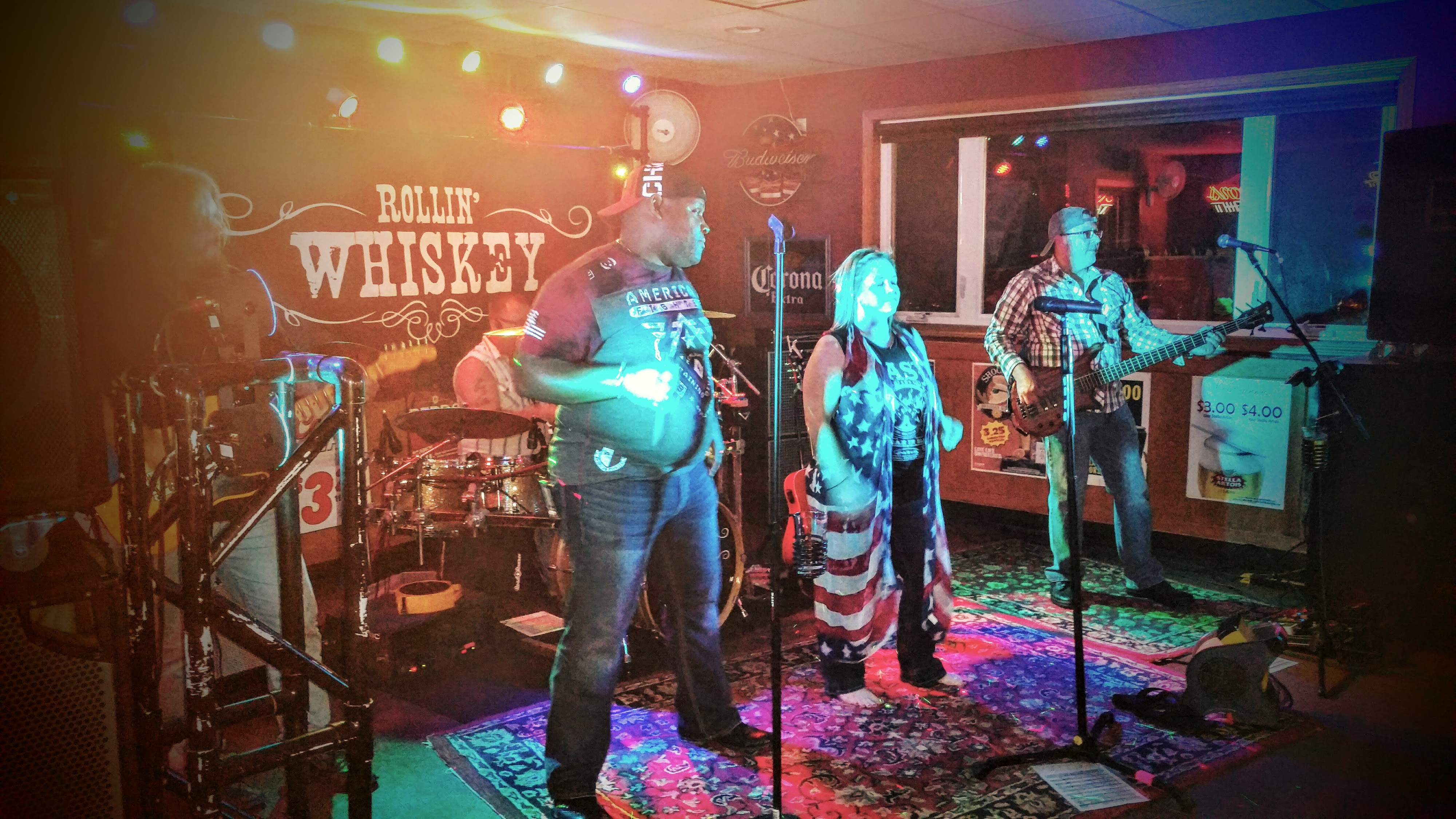 A live band named Rollin' Whiskey performs on a small stage under colorful lights in a lounge.