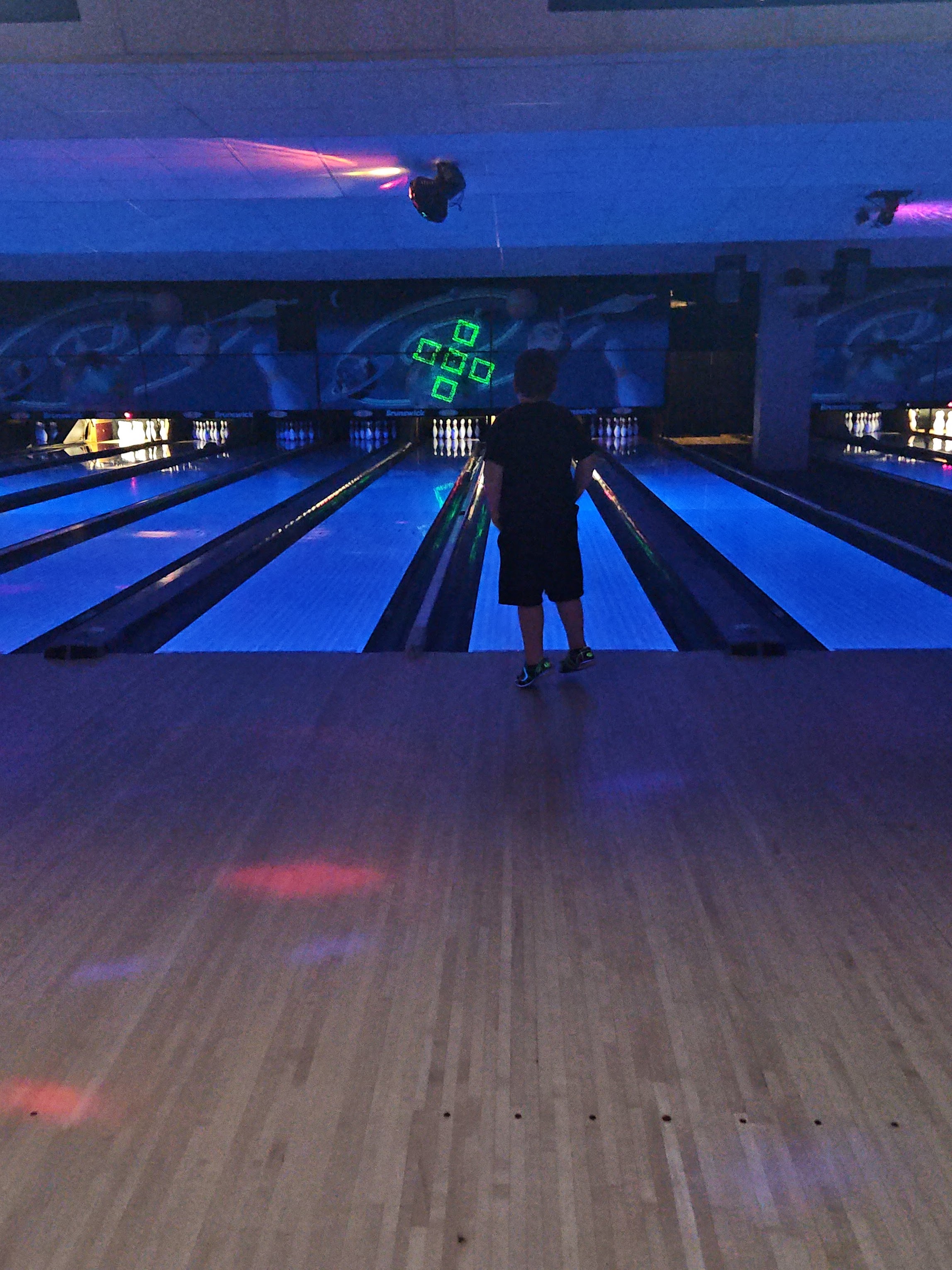 A person stands at the start of a bowling lane under vibrant blue cosmic lighting.