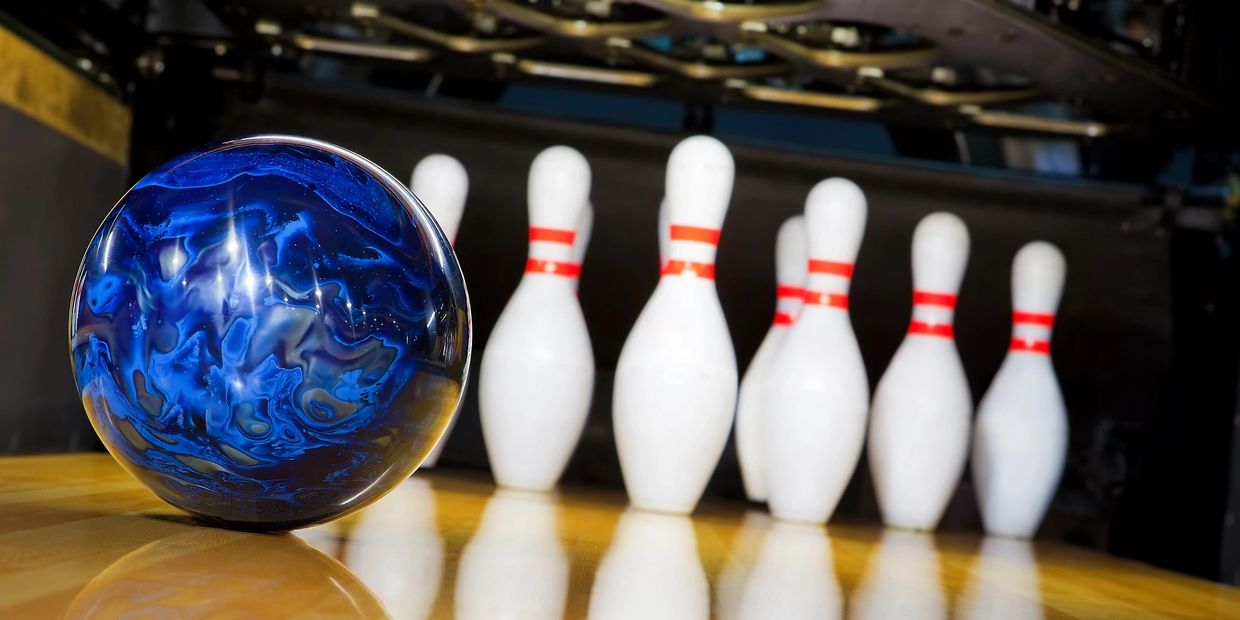 A close-up of a blue marbled bowling ball on a glossy lane with pins in the background.