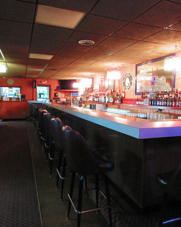A long wooden bar with black stools and a well-stocked back bar under warm lighting.