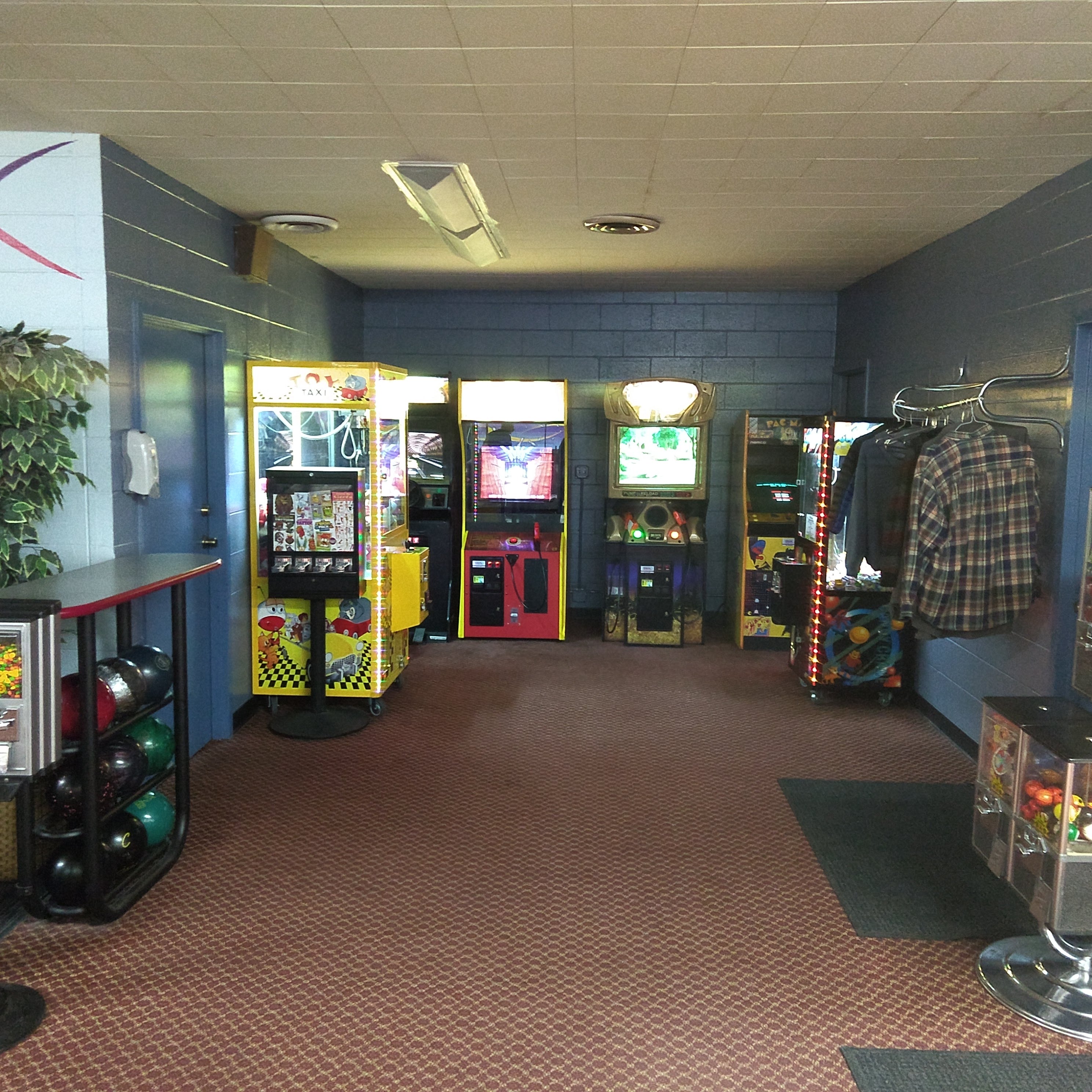 An arcade area with various game machines, a bowling ball rack, and blue cinder block walls.