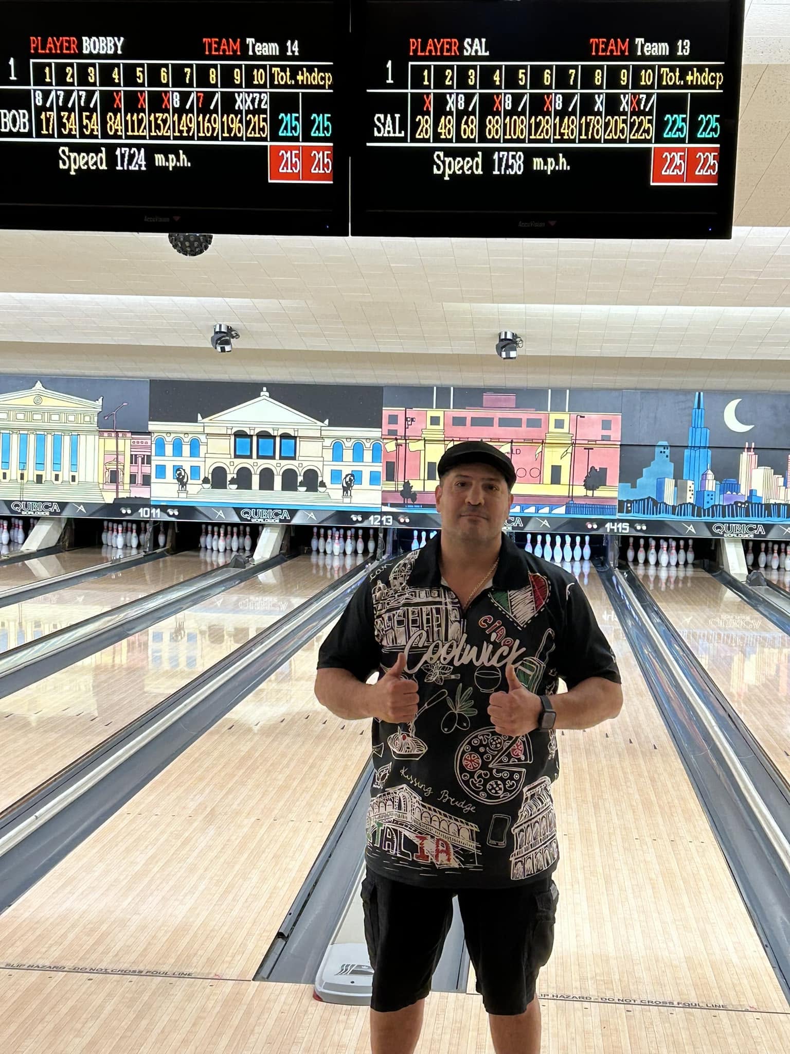 A man in a themed bowling shirt giving thumbs up in front of bowling lanes and high-score monitors.