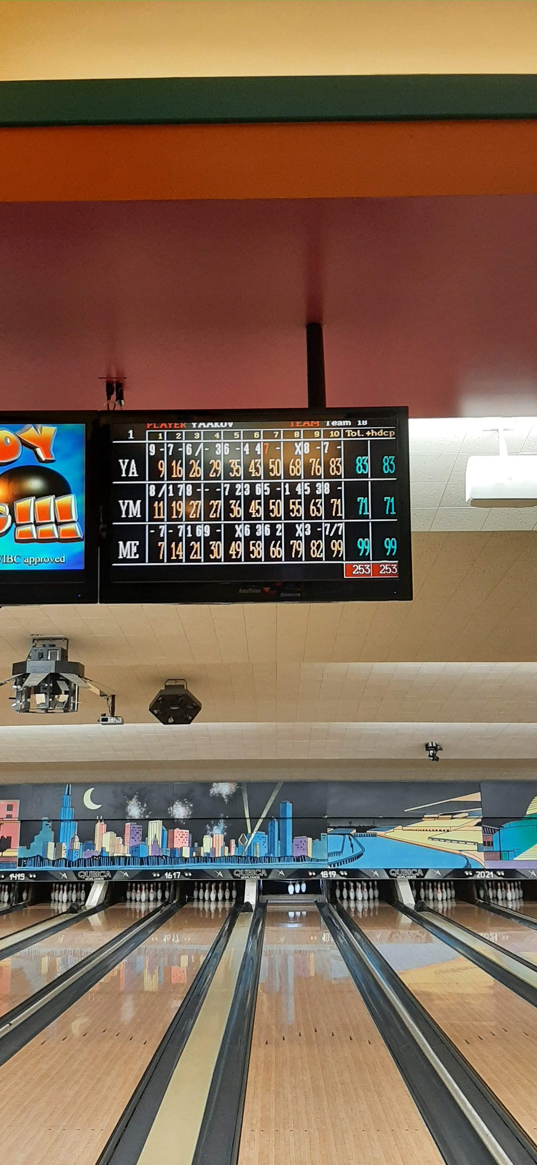 A vertical view of bowling lanes at Habetler Bowl featuring an overhead digital scoreboard and Chicago skyline murals.