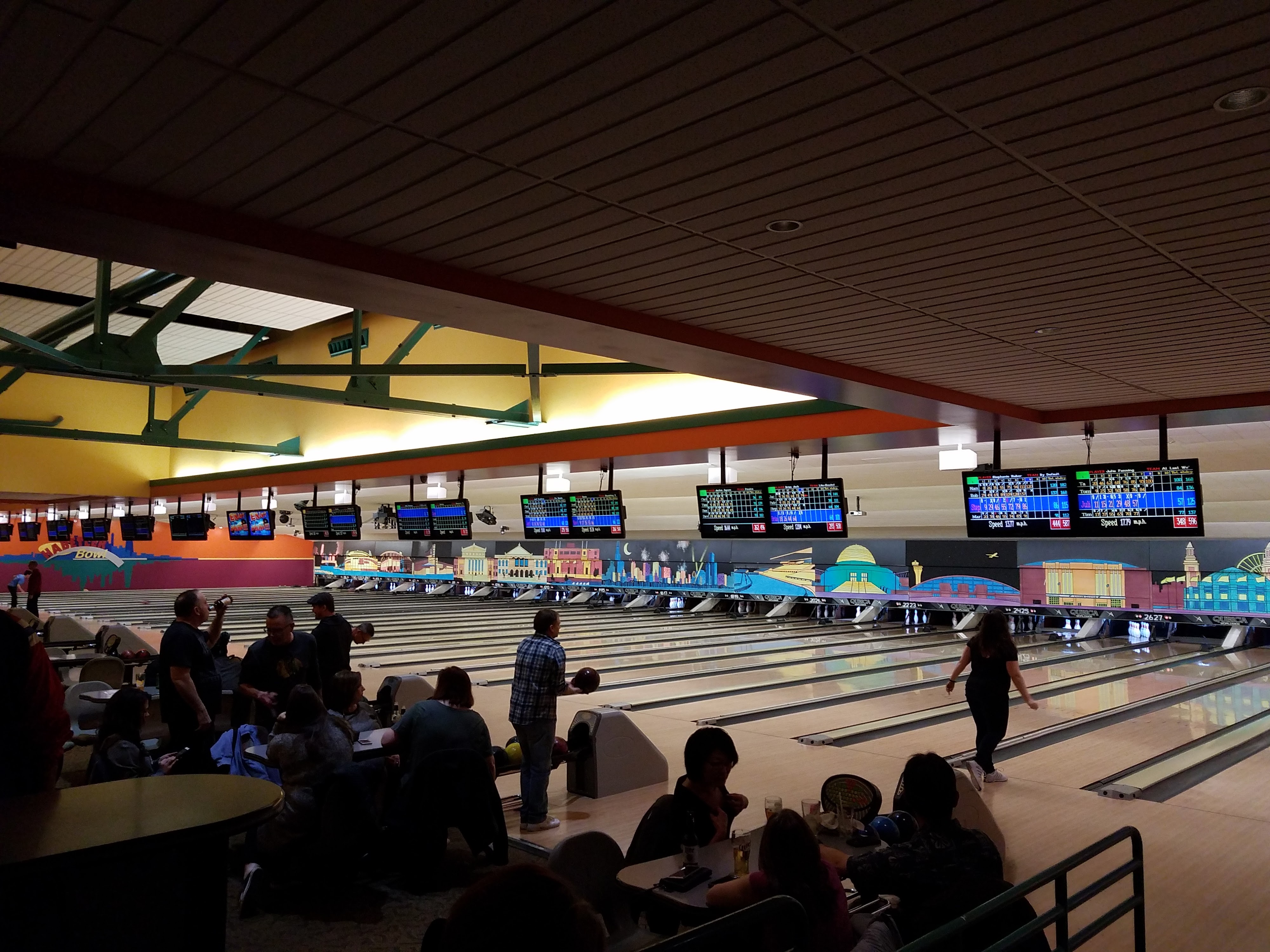 A wide view of people bowling at Habetler Bowl with colorful murals and overhead scoring monitors.