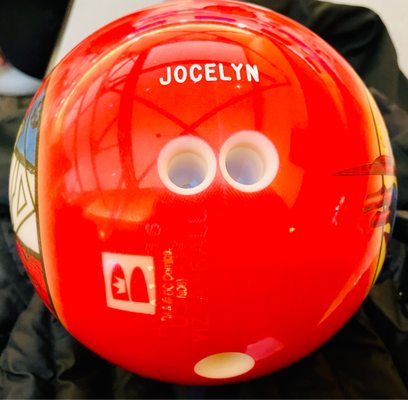A red personalized bowling ball with the name Jocelyn printed in white above the finger holes.