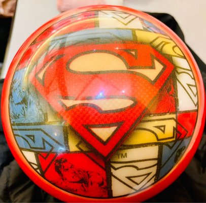 A close-up of a red and white bowling ball featuring Superman comic book graphics and the iconic S logo.