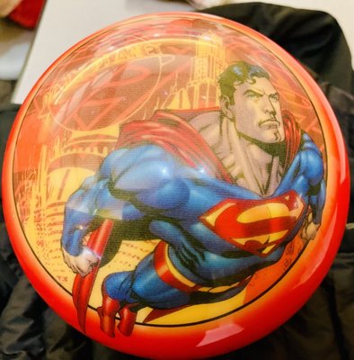 A red bowling ball featuring a graphic of Superman flying in front of a city backdrop.