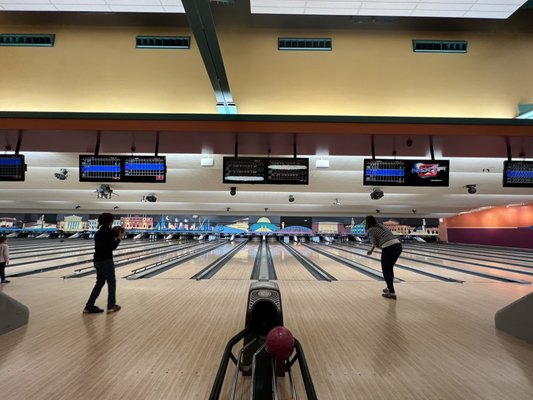 Wide view of several bowling lanes with two people playing and digital scoring monitors overhead.