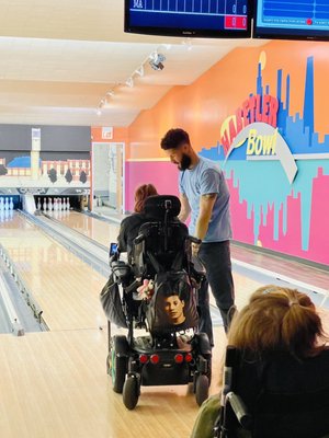 A man assists a person in a power wheelchair on a bowling lane at Habetler Bowl.
