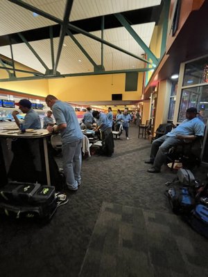 Bowlers in matching blue shirts gather in the concourse area with their equipment bags.