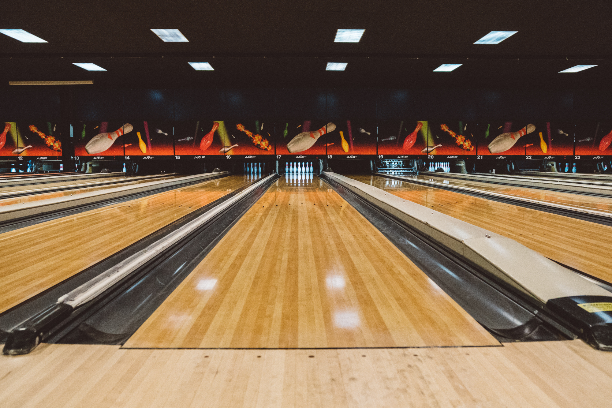 A low-angle view of multiple polished wood bowling lanes under bright indoor lighting.