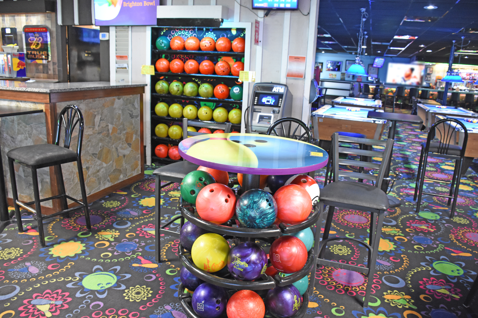 The interior of a bowling center lounge with a colorful ball rack, bar seating, and billiard tables.