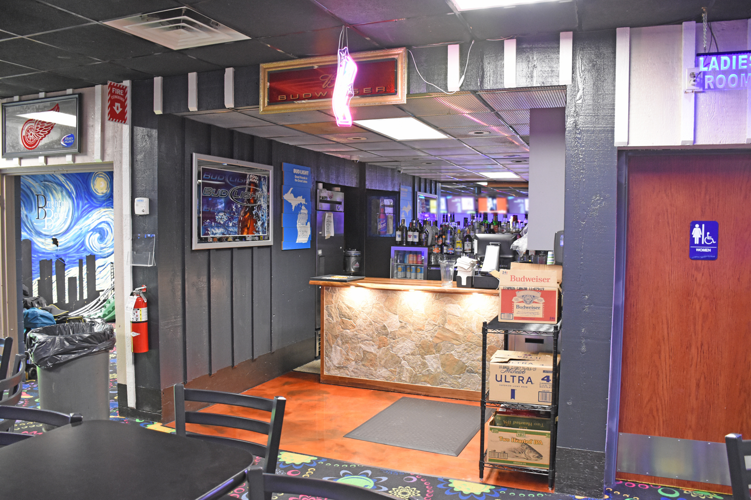 A stone-faced bar counter in a bowling center with beer signs, a colorful mural, and seating.