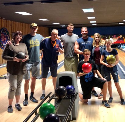 A group of eight people smiling and holding bowling balls while posing on a bowling lane.