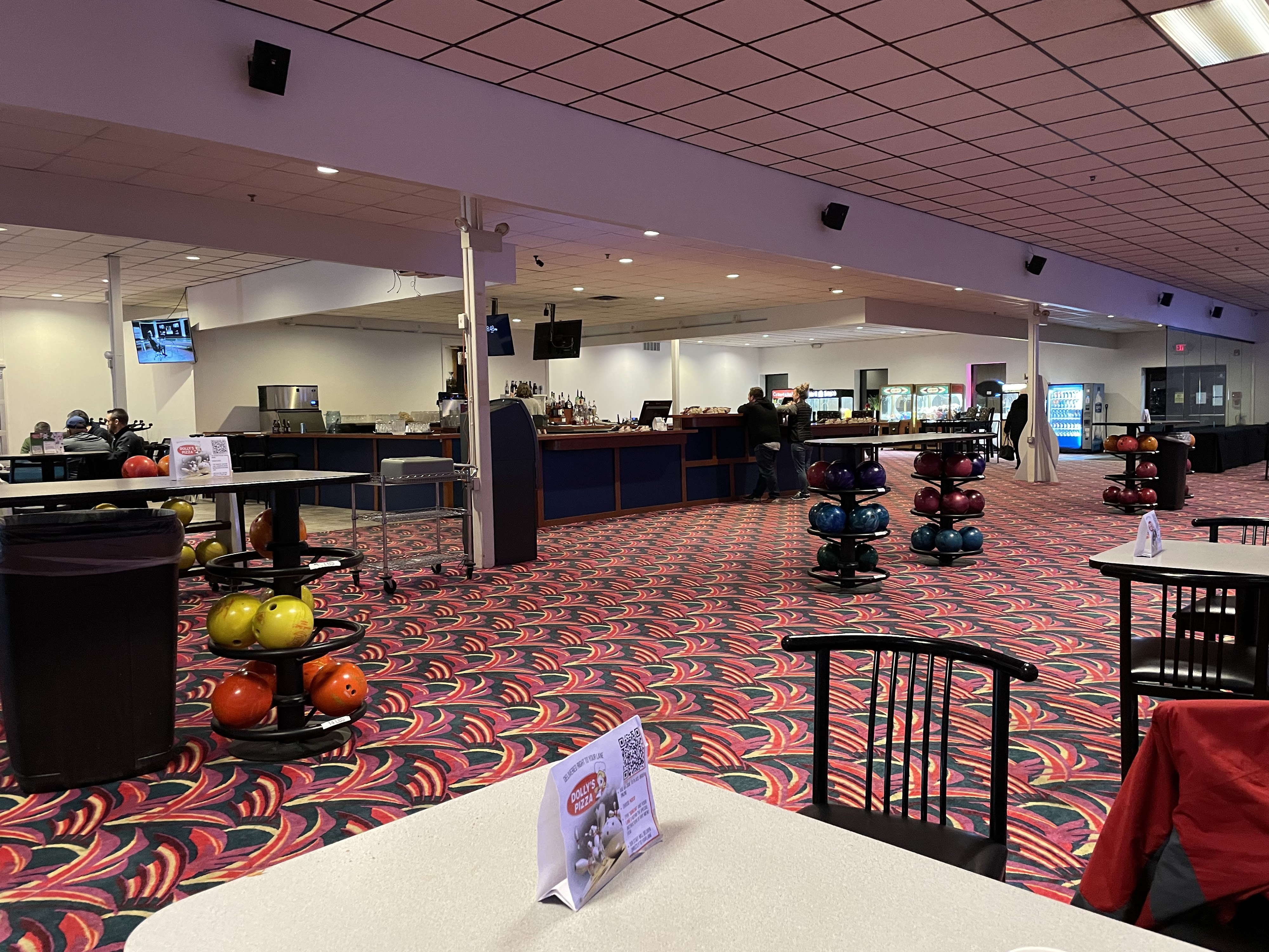 Interior view of a bowling center concourse featuring a large bar, ball racks, and vibrant patterned carpet.