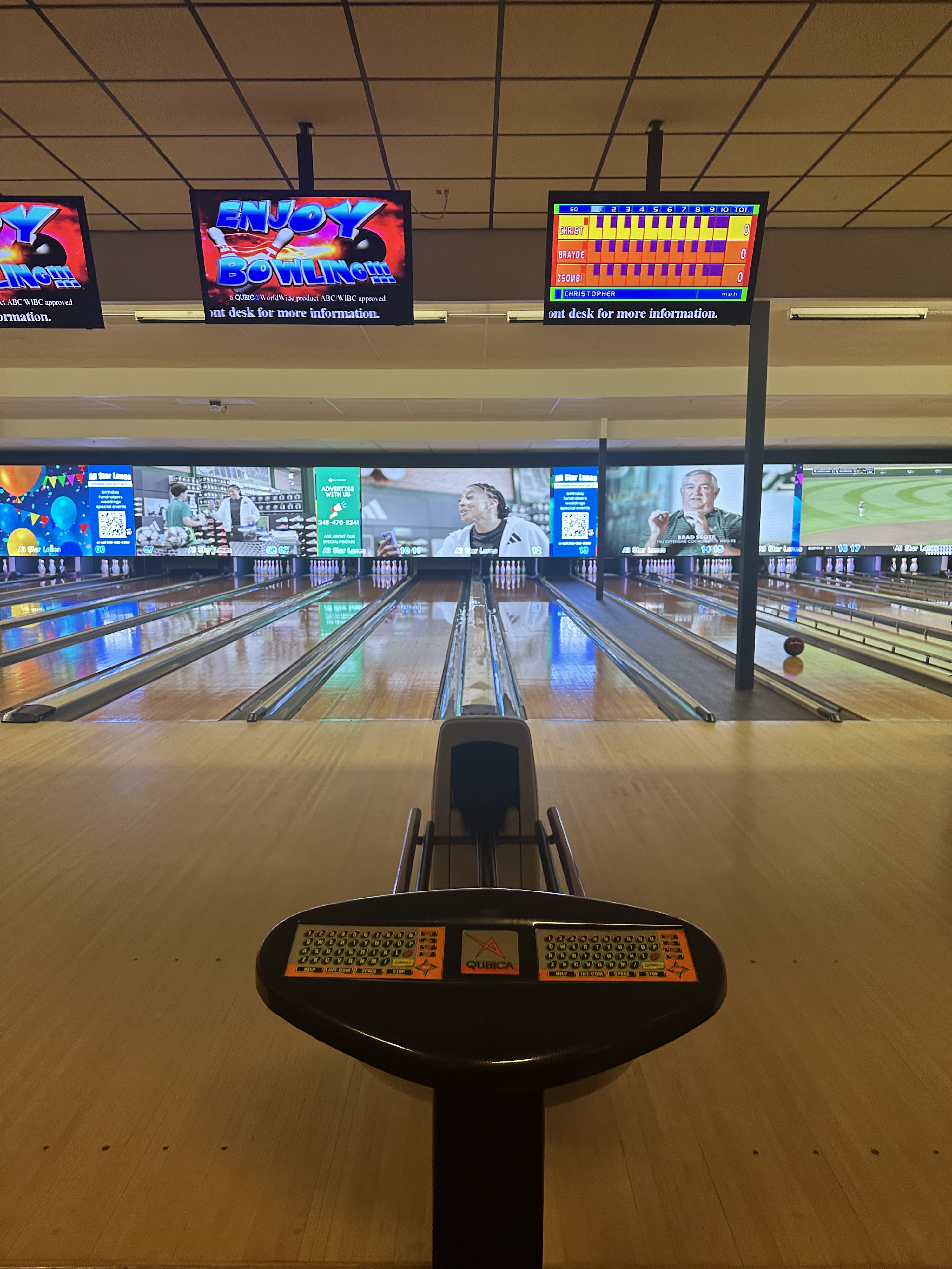 A first-person view from a bowling scoring console looking down several polished wooden lanes under bright lights.