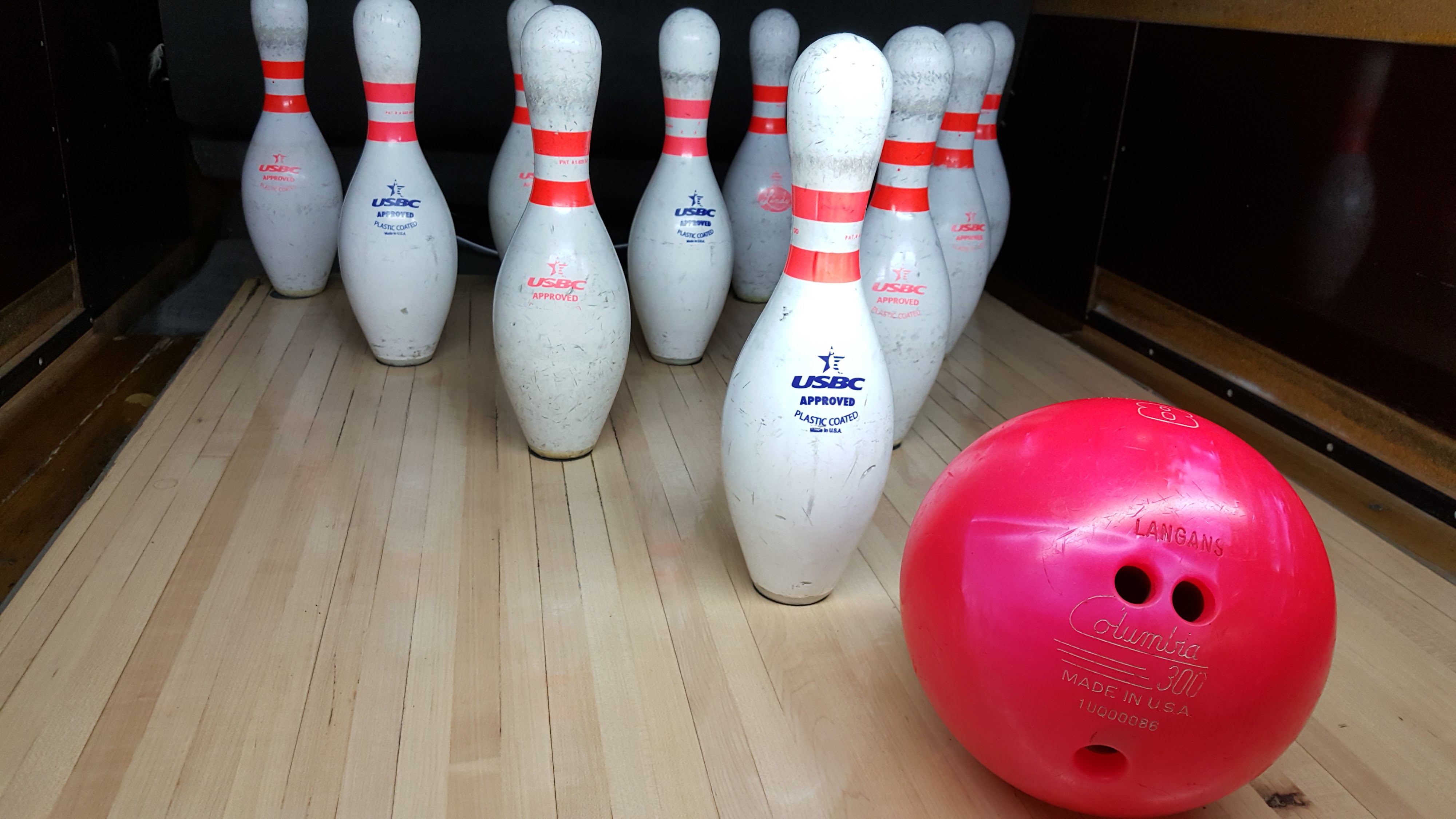 Close-up of ten white bowling pins and a bright pink bowling ball on a wooden lane.