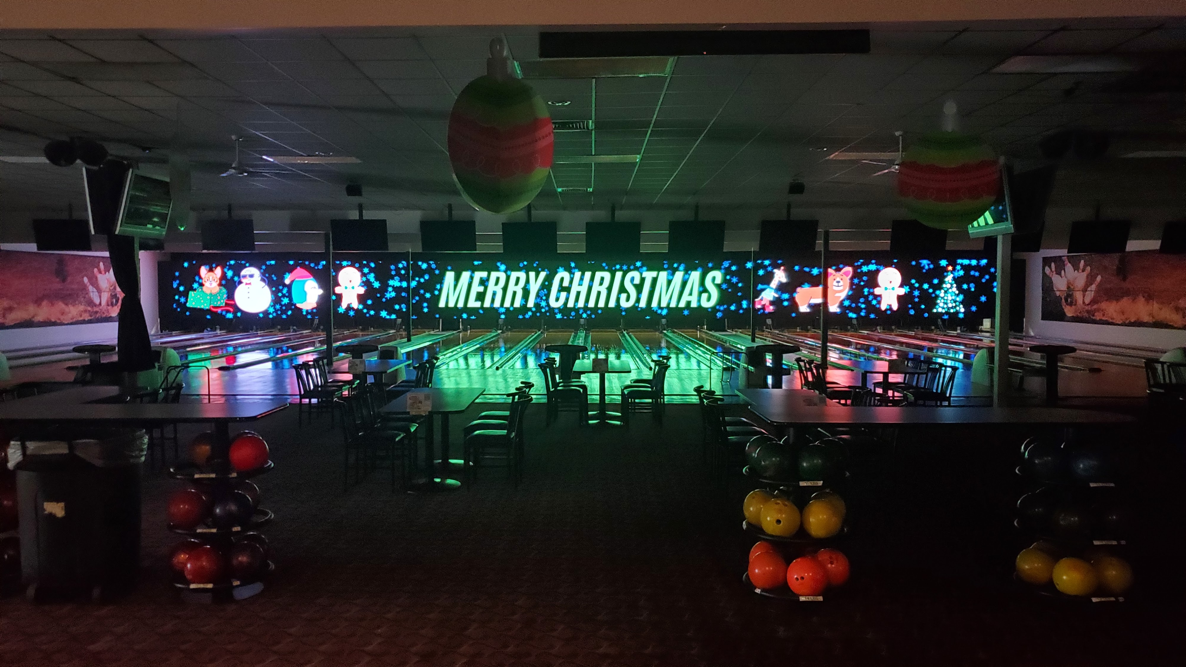 Indoor bowling lanes at night with a large LED screen displaying Merry Christmas and festive holiday graphics.