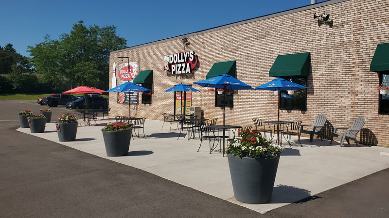 Outdoor patio at All Star Lanes with umbrella-covered tables and Dolly's Pizza signage on a sunny day.