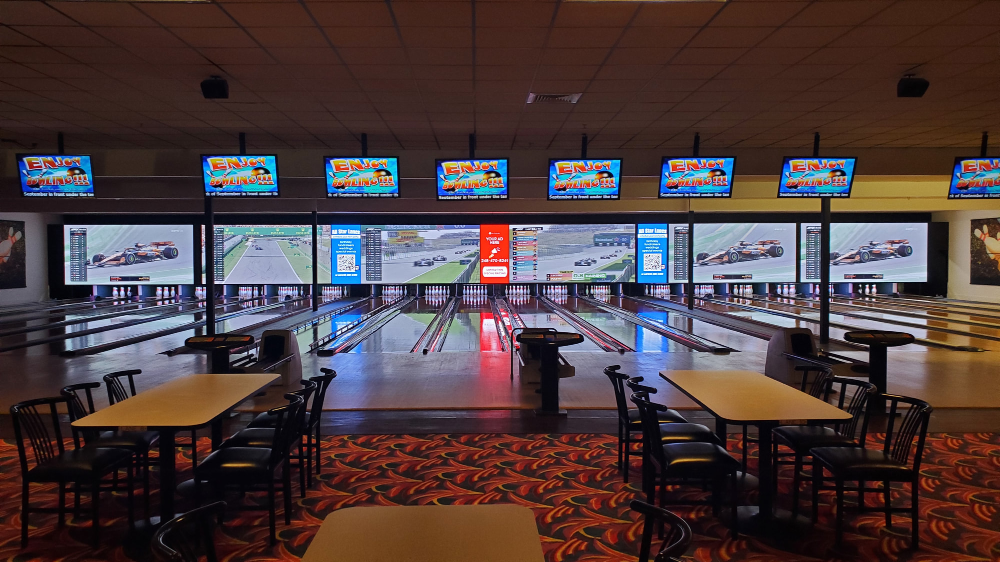 Wide view of modern bowling lanes with large video screens and overhead scoring monitors.