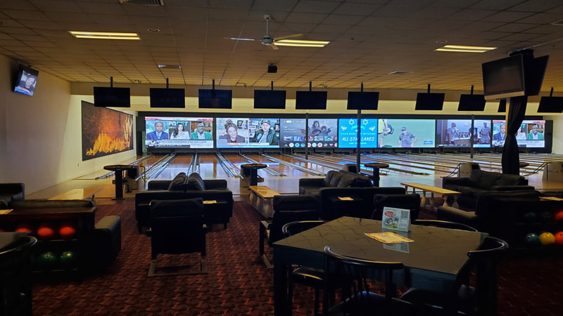 Modern bowling center interior with leather sofas and large digital screens at the end of the lanes.