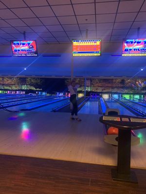 A person stands on a bowling approach under blue cosmic lighting with overhead scoring monitors.