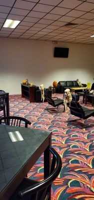 A lounge room with black leather seating and colorful patterned carpet decorated with Halloween skeletons.