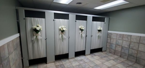 Four bathroom stalls decorated with white fabric and flower bouquets.