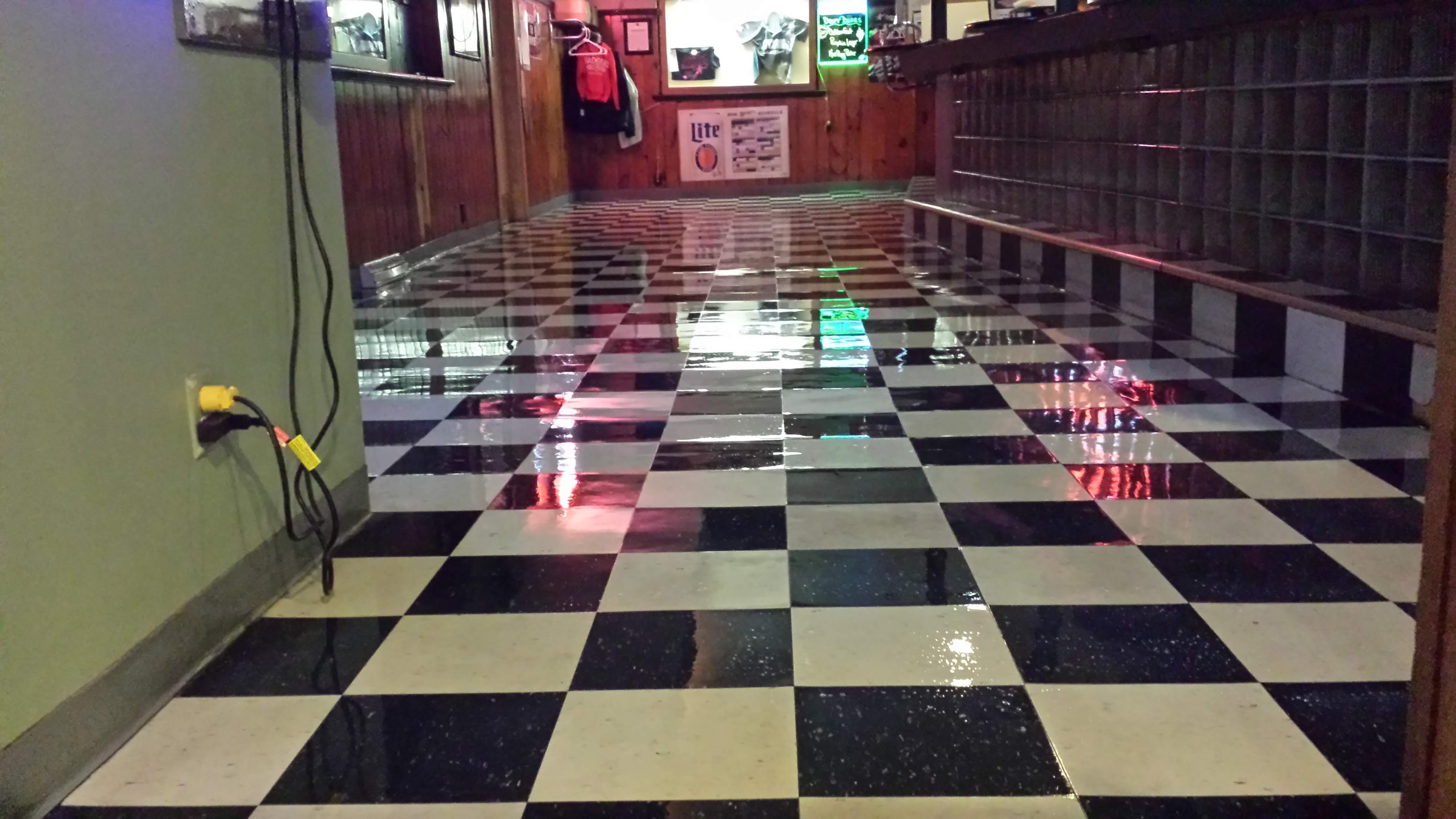 A hallway with a wet, reflective black and white checkered floor, wooden paneling, and dark locker cubbies.