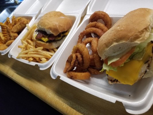 Three take-out containers filled with fried food including a burger, chicken sandwich, and various fries.