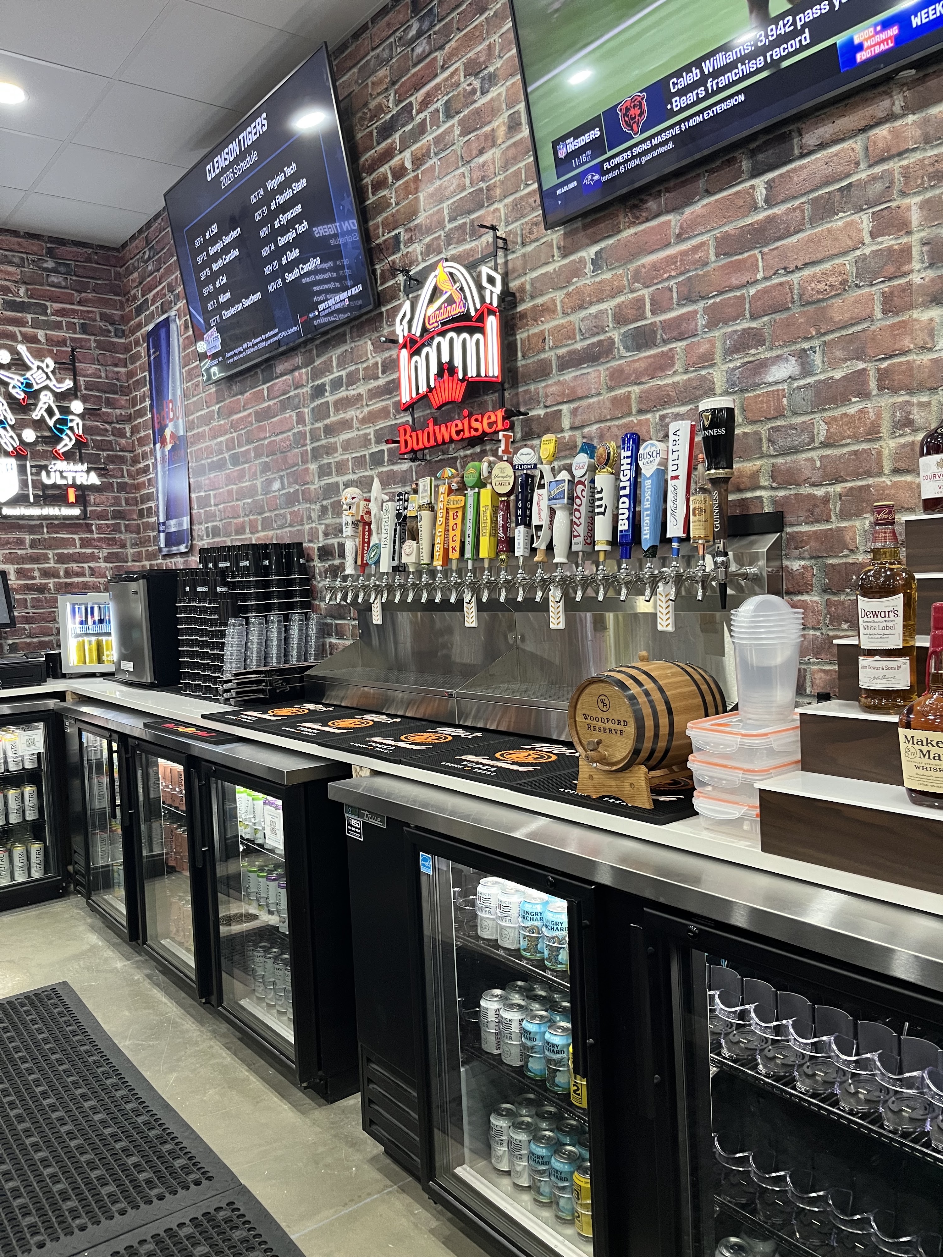 A modern bar with a brick wall, multiple beer taps, sports televisions, and beverage coolers.