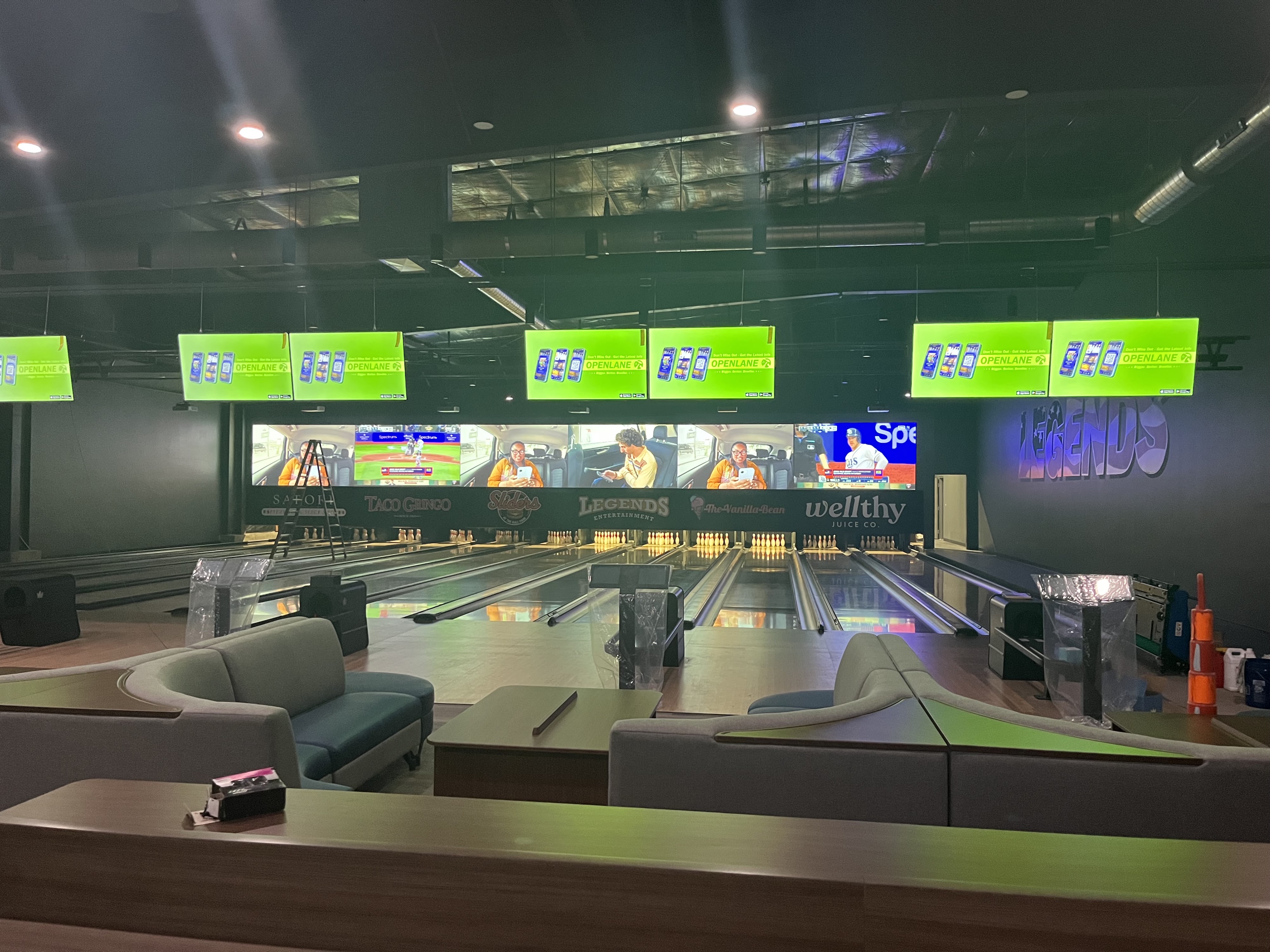 Modern bowling lanes with curved sectional seating, digital scoreboards, and video walls showing sports broadcasts.