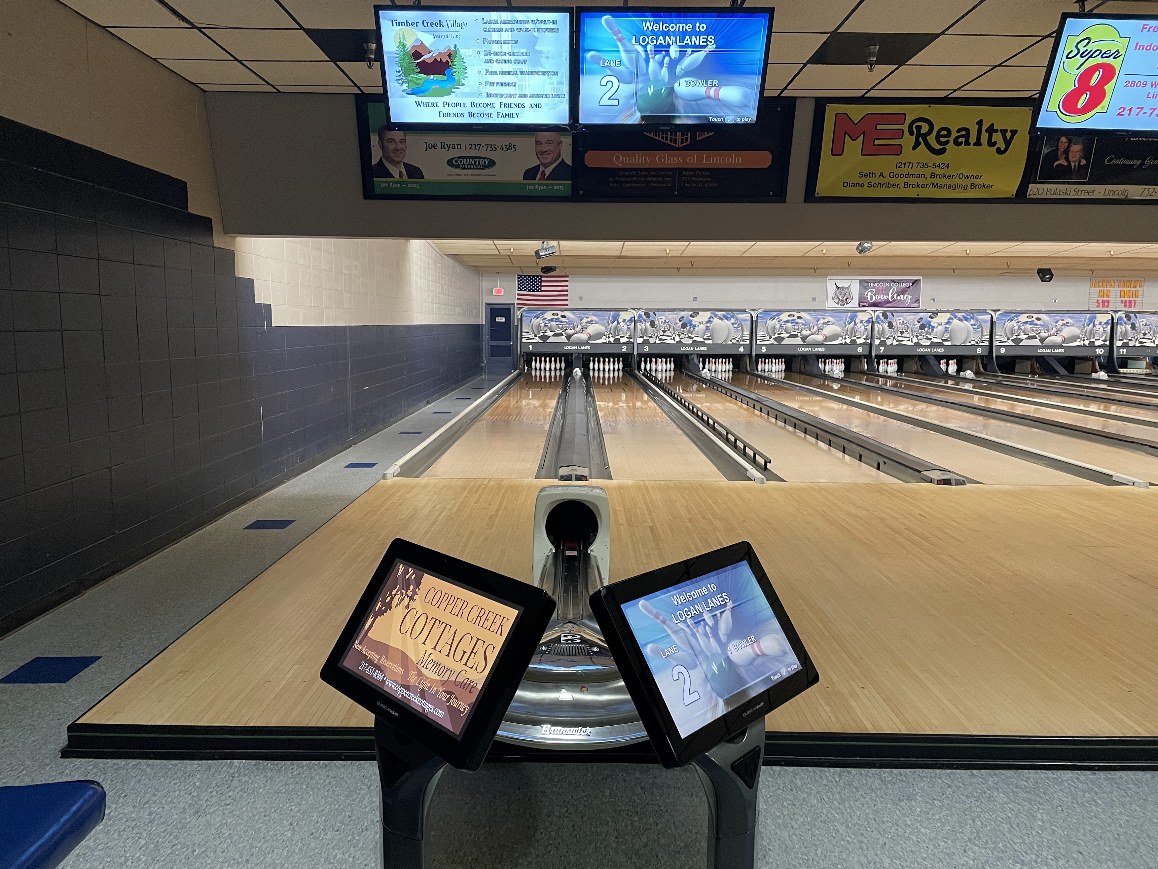 View down a clean, brightly lit bowling lane with automatic scoring screens and multiple lanes receding into the distance.