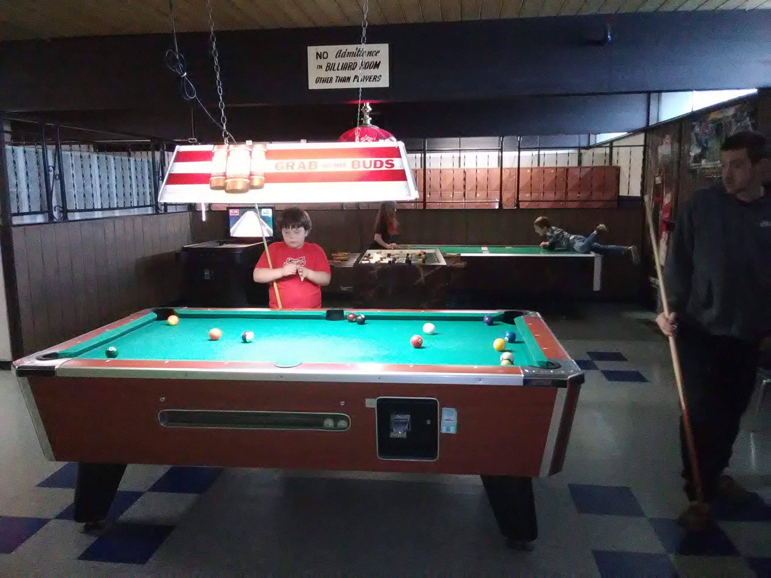 Child in red shirt plays pool at a turquoise-felt table in a recreation room at Logan Lanes.