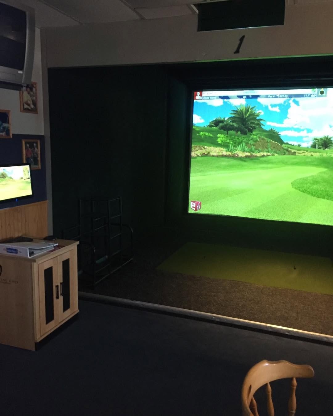 Dark party room with golf simulator on projection screen and wooden cabinetry.