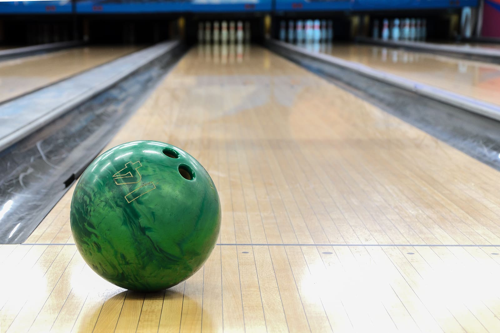 Green bowling ball on a polished lane with additional lanes visible in soft focus behind it.