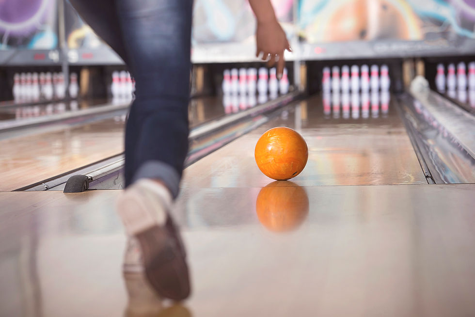 A person bowls an orange ball down a lane toward pins.