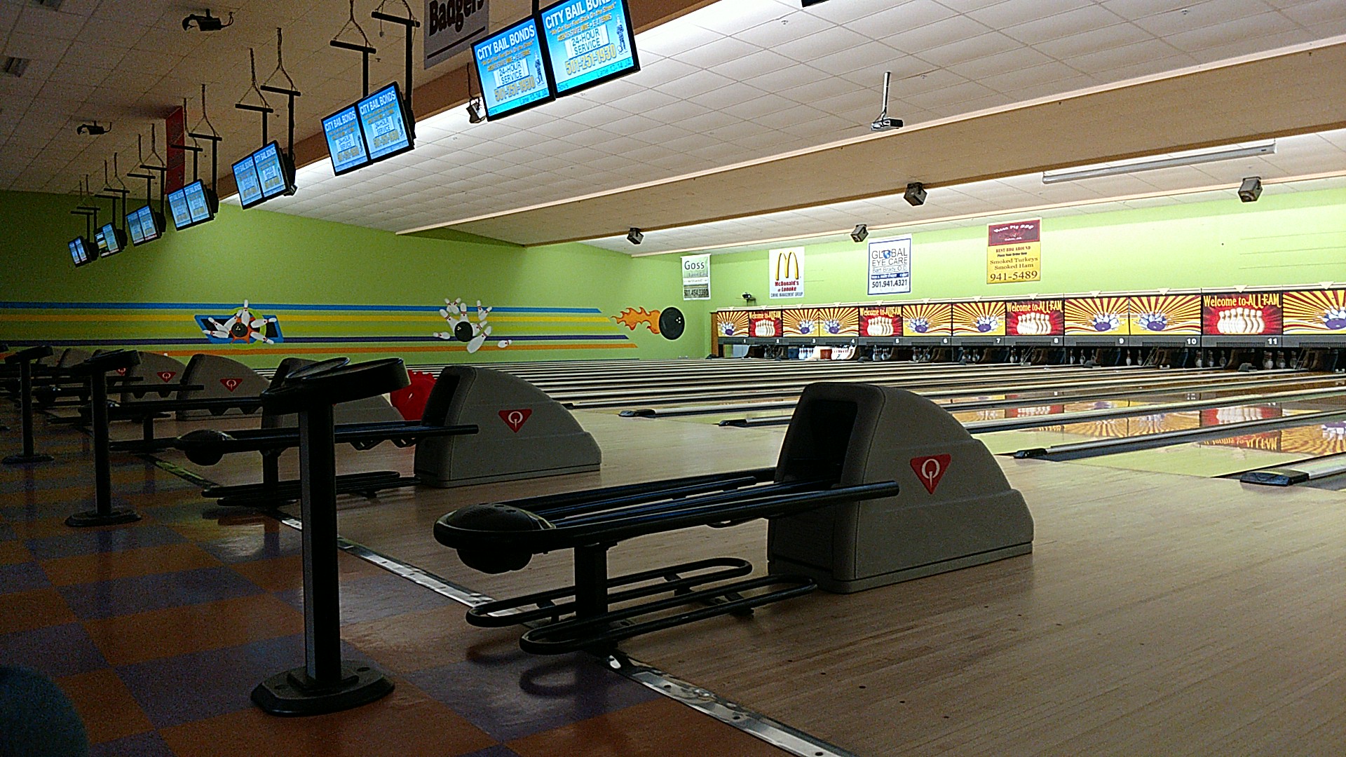 A wide-angle view of clean bowling lanes with gray ball returns and overhead monitors at Allfam Bowling.
