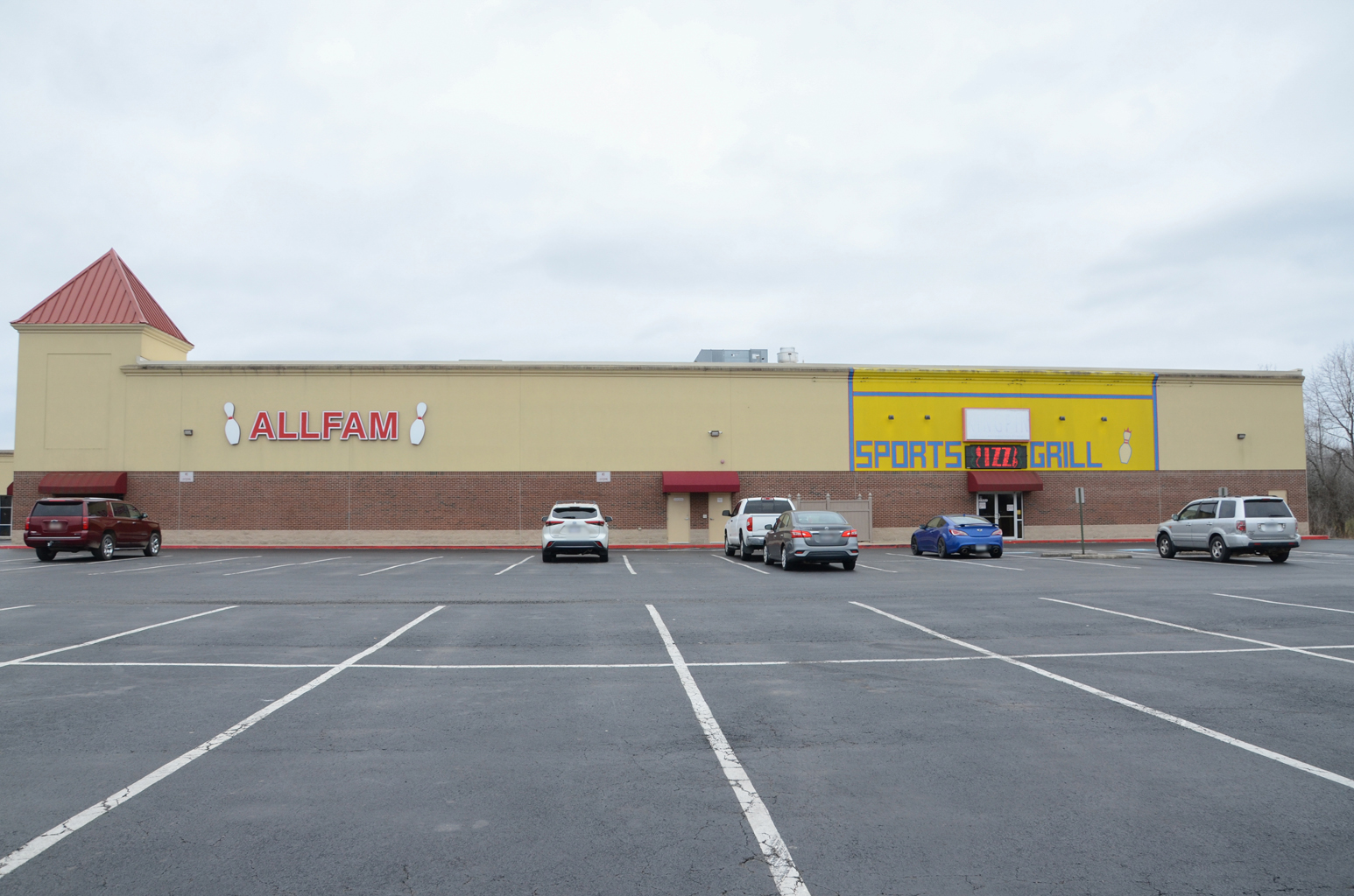 Exterior view of the Allfam Bowling and Entertainment Center building and parking lot under a cloudy sky.