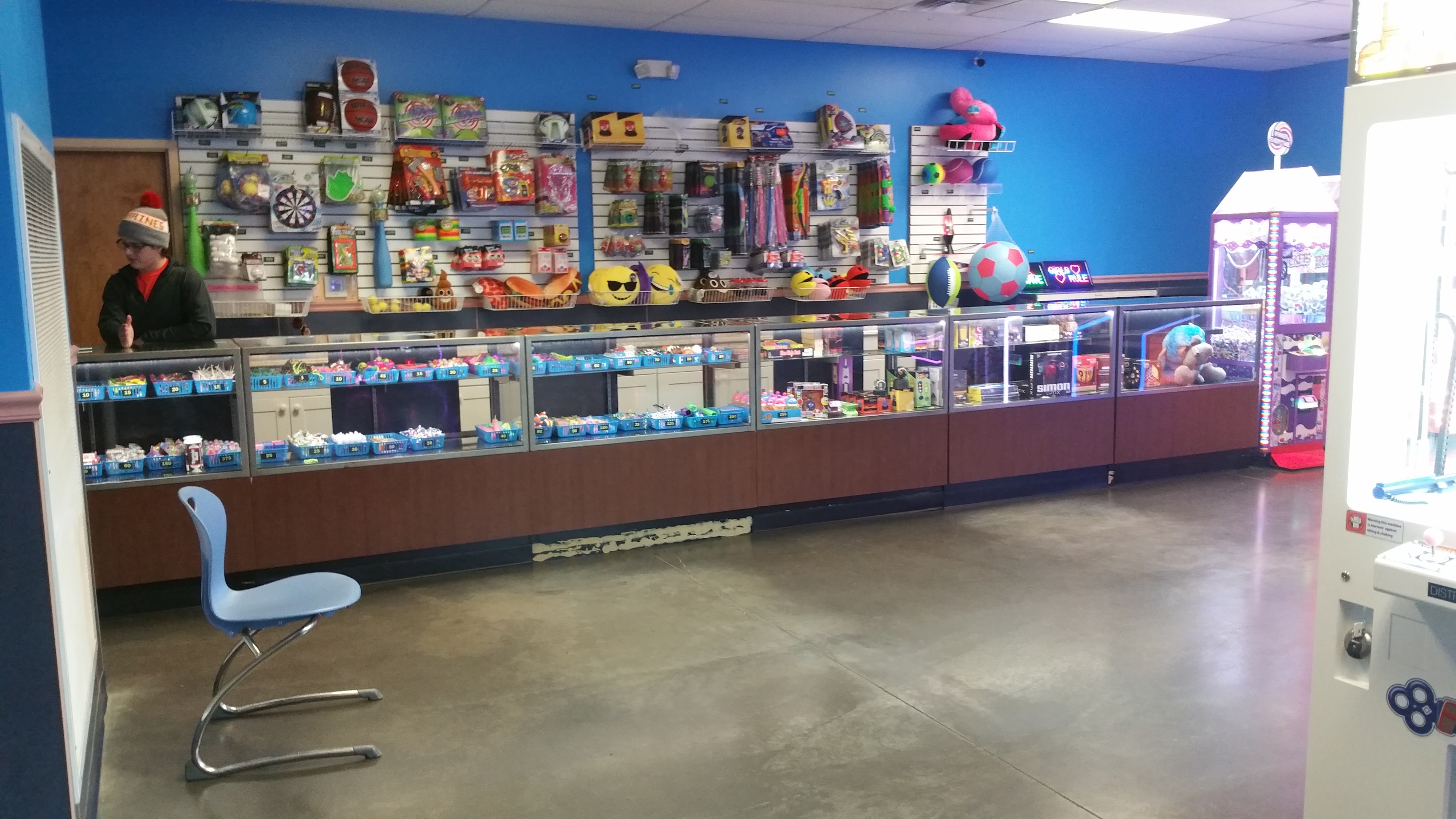 An arcade redemption counter with glass display cases and shelves stocked with various toys and prizes.