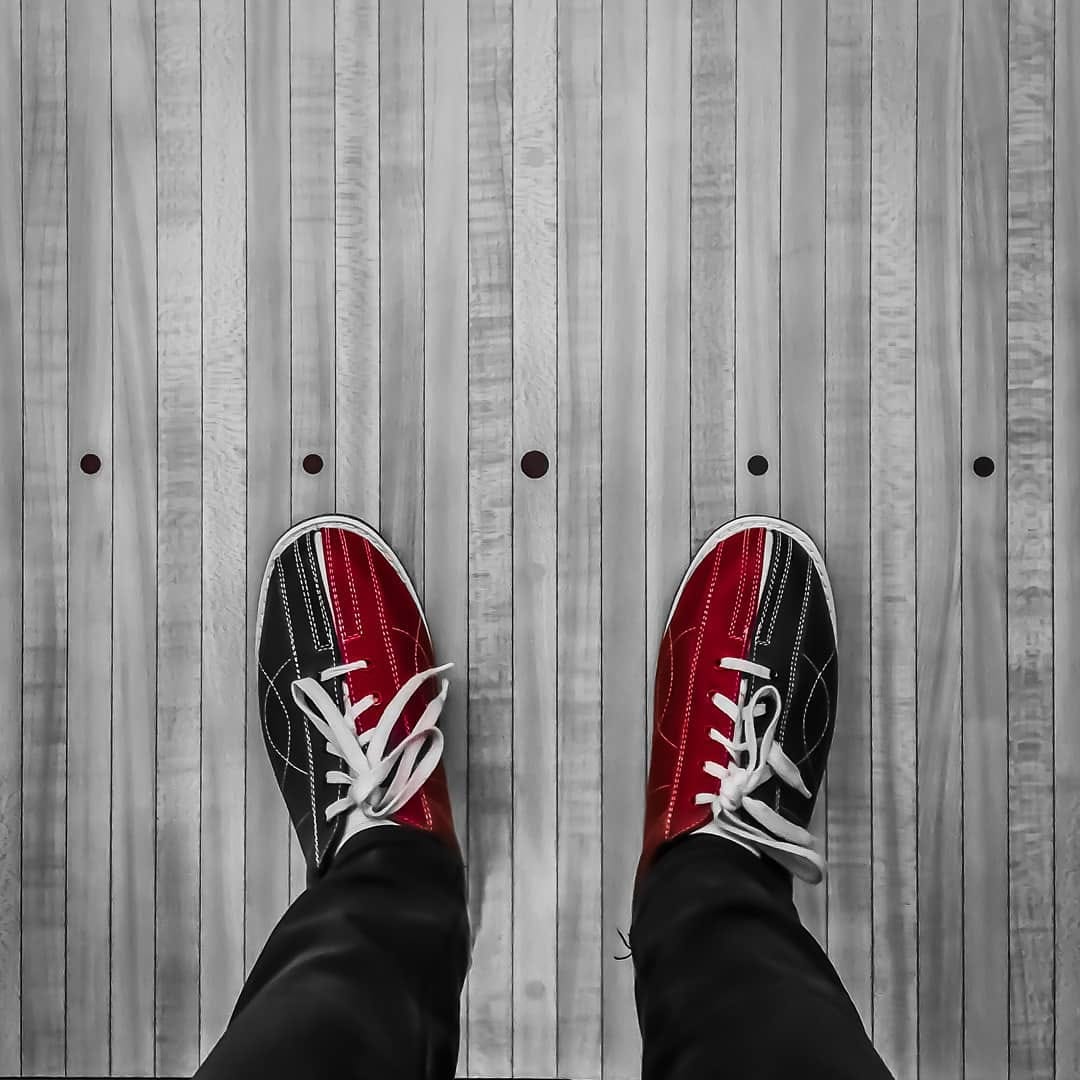 Overhead view of red and black bowling shoes standing on a wooden bowling lane approach.