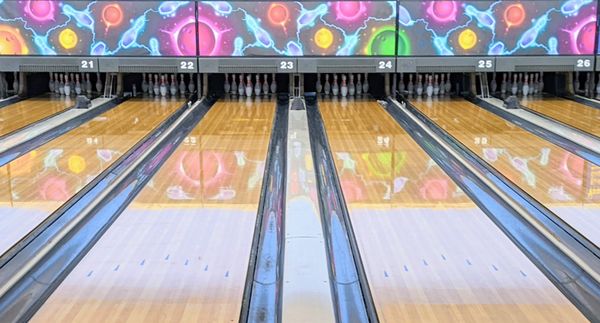 Symmetrical view of six polished wooden bowling lanes with colorful cosmic-themed graphics above the pins.
